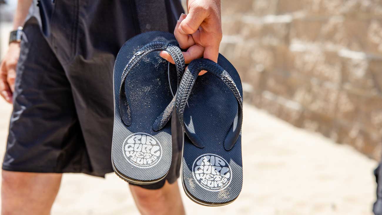 A grom carrying a pair of black Rip Curl thongs