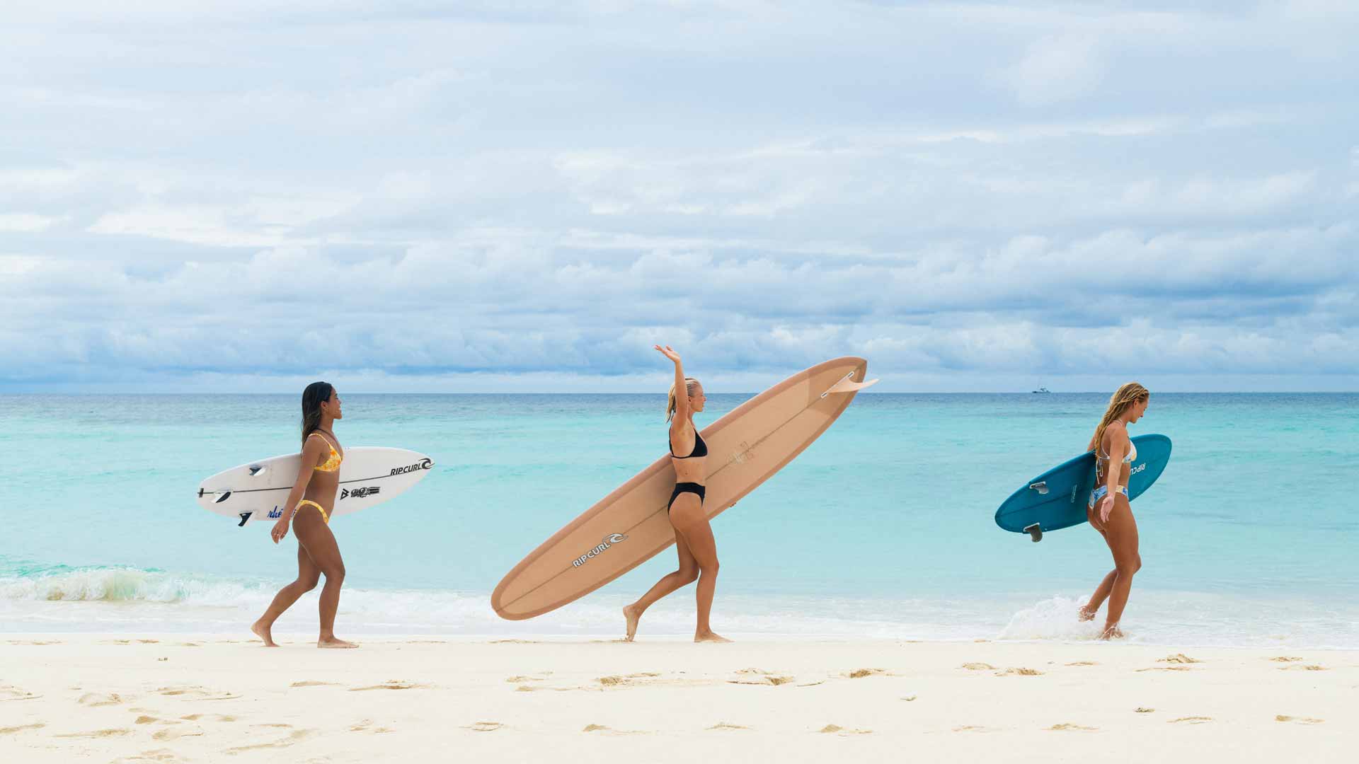 Rip Curl women walking along the beach carrying their boards