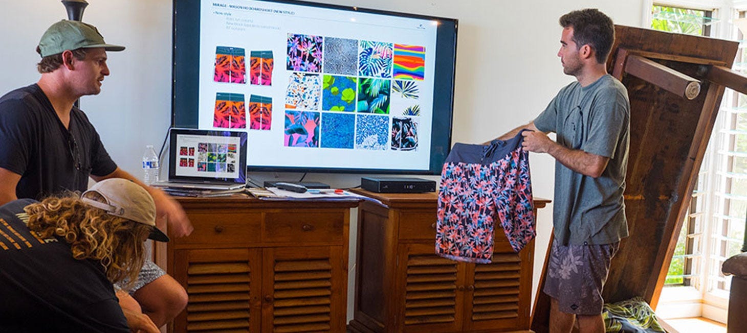 Rip Curl Crew looking at boardshort patterns on a screen while holding up a boardshort prototype and comparing