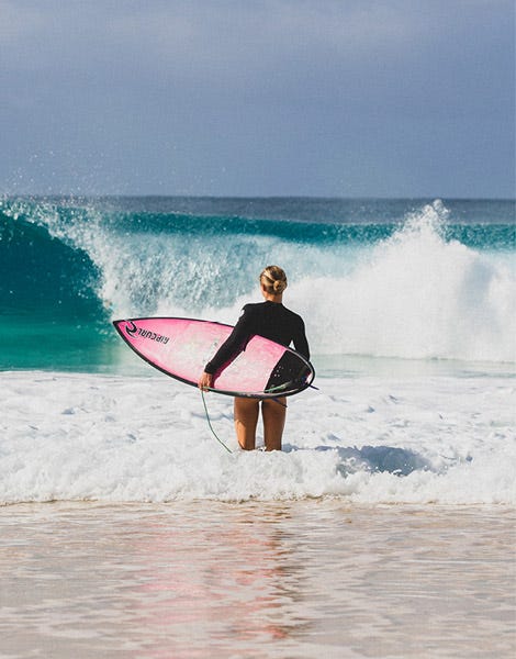 Alyssa Spencer carrying her surfboard standing in the shallow water