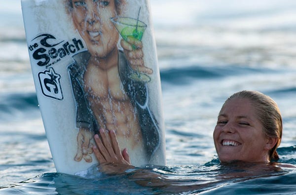 Stephanie Gilmore in the water holidng her surfboard in the air